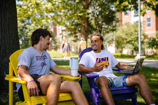 Two students sitting in the adirondack chairs on campus.